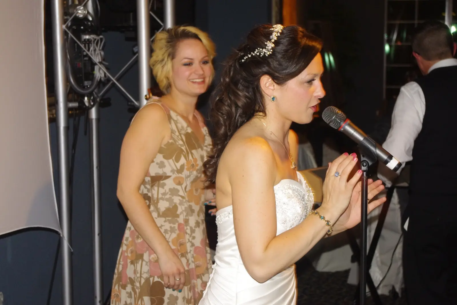 A bride singing into the microphone while her guests look on
