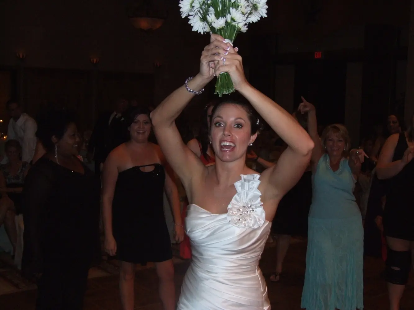 A bride raising her bouquet while celebrating with her guests