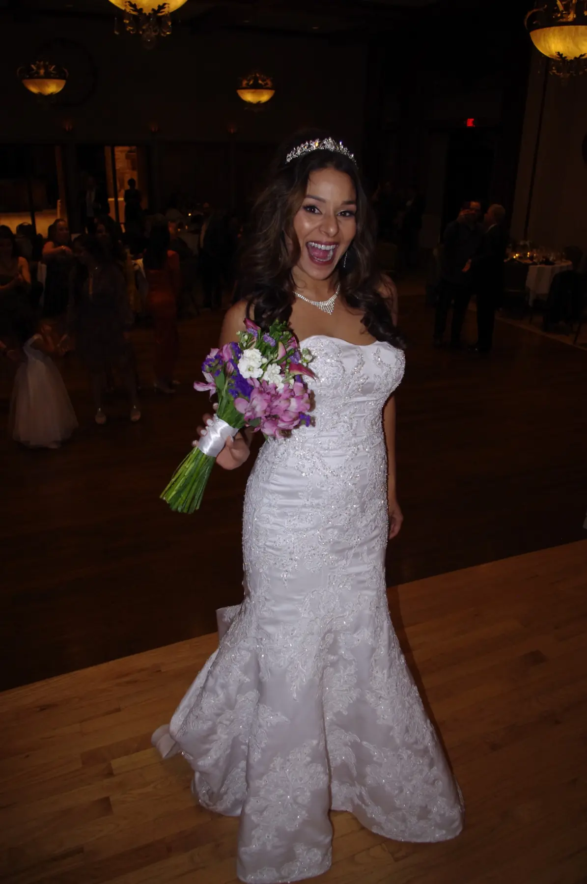 A bride smiling on the dance floor while holding her bouquet